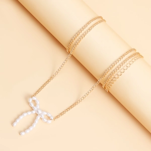 Chaîne de corps dorée élégante avec pendentif nœud en perles blanches sur socle beige