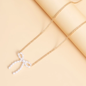 Détail d'une chaîne de taille dorée avec pendentif nœud en perles sur socle beige