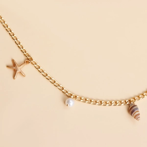 Détail de la chaîne de taille bohème dorée avec pendentifs étoile de mer, perle et coquillage