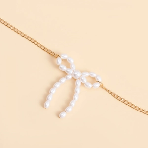 Détail d'une chaîne de taille dorée ornée d'un pendentif nœud en perles blanches