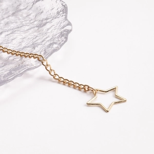 Close-up of gold star body chain with hollow pentagram pendant on white background