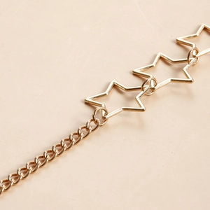 Macro shot of gold hollow star links on metal body chain against beige texture