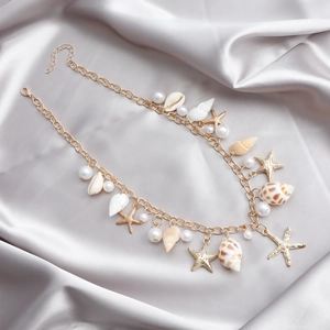 Détail d'une chaîne de taille bohème dorée avec coquillages, étoiles de mer et perles