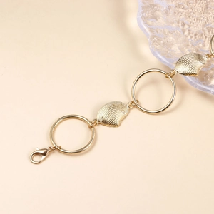 Détail de breloques coquillages dorées et anneaux métalliques sur une chaîne de corps
