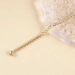 Détail d'une chaîne d'extension dorée avec un pendentif boule métallique lisse et poli