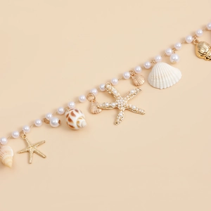 Gros plan des pendentifs coquillage, étoile de mer et perles sur une chaîne de corps