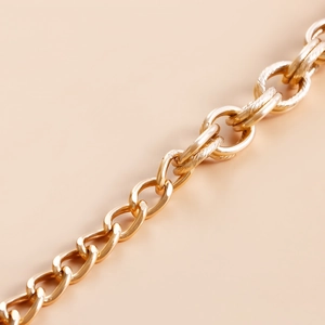 Detailed close-up of thick gold metal body chain with smooth and engraved oval links