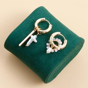 Macro detail of asymmetric gold earrings with white cross pearl and small pink beads