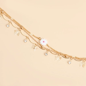 Macro detail of gold multi-layer chain with crystal butterfly and daisy charms