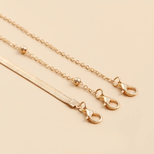 Detail of layered gold metal waist chains featuring snake link and bead strands with lobster clasp