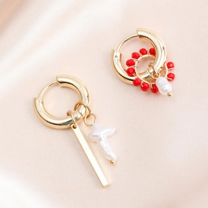 Detail of asymmetric gold earrings with pearl cross and red bead woven charms