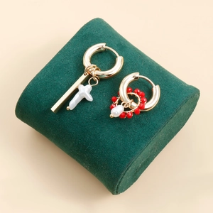 Detail of asymmetric gold hoop earrings with white pearl cross and red beaded accents