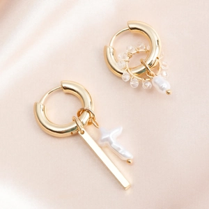 Detail view of asymmetric gold earrings with pearl cross and geometric beaded charms