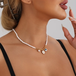 Detail of white beaded necklace featuring a golden letter A and blue evil eye charms