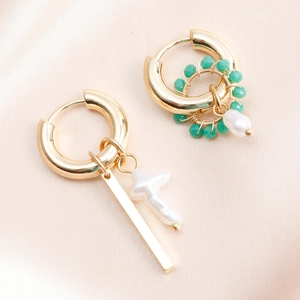 Detail of asymmetric gold earrings with turquoise beads, cross and baroque pearl charms