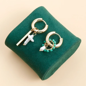Asymmetric gold earrings with cross pearl and green beads on green velvet stand