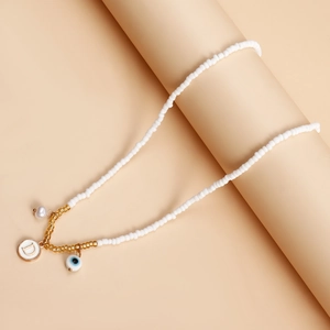 Detail of white beaded necklace with golden letter D, evil eye, and pearl charms