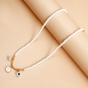 Detail of beaded necklace with evil eye, pearl, and letter V pendant on pink background