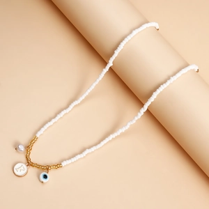 Detail of white beaded necklace with blue evil eye, faux pearl, and letter F pendant
