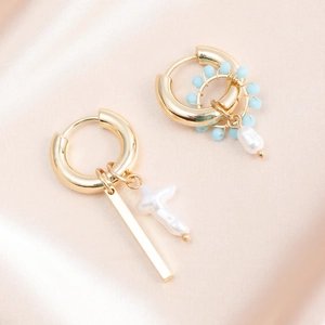 Macro shot of gold geometric earrings with pearls and blue beads on silk fabric