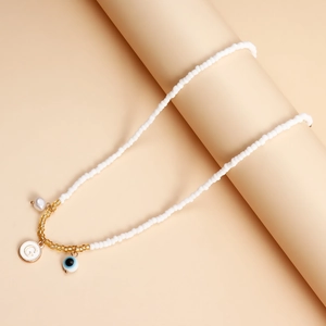 Detail of white bead necklace featuring a pearl, letter G tag and evil eye pendant charm