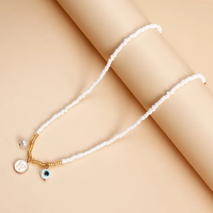 Detail of white beaded necklace with Evil Eye charm and gold letter W pendant on a prop