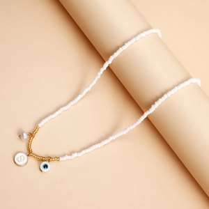 Detail of white seed bead necklace with gold S letter and evil eye charms on a stand