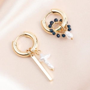Detail of asymmetric gold hoop earrings with cross-shaped pearl and blue beaded drop