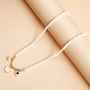 Detail of white beaded necklace with gold accents, letter B disc and blue evil eye charms
