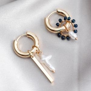 Detail of asymmetric gold earrings with blue beads and baroque pearls on silver satin fabric