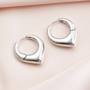 Détail macro de créoles cœur en argent poli sur fond en soie rose élégante
