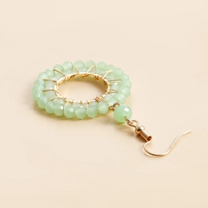 Detailed close-up of light green crystal beads woven on a golden circular hoop earring
