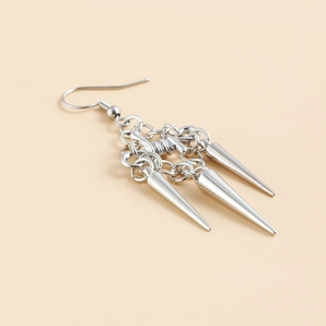 Macro detail of gothic silver long tassel rivet earrings with triple metal cone pendants