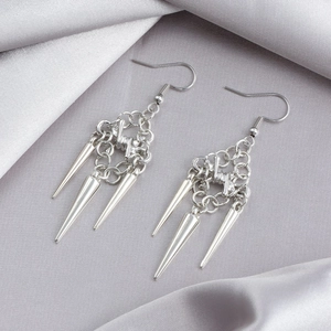 Macro detail of silver gothic earrings with spiked tassels on grey silk fabric backdrop