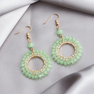 Close-up of light green crystal beads hand-woven on golden circular drop earrings