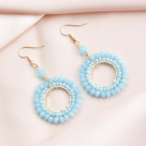 Close-up of light blue beaded hoop earrings with gold woven wire on pink silk background