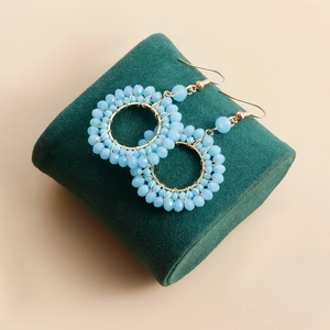 Detailed view of light blue faceted beaded hoop earrings on a green velvet display stand