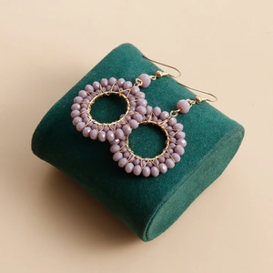 Detail of handmade woven purple crystal beads on golden circular drop earrings