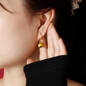 Close-up of golden Christmas bell earrings featuring a polished mirror finish on model