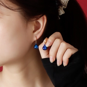 Detail of blue bell charms on golden hoop earrings worn by a model on a red background