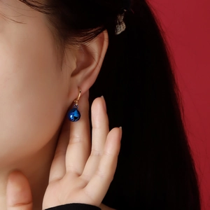 Close-up of blue bell earrings with gold hoop and heart cutout on a red background