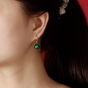 Close-up of model wearing a green bell charm earring with heart cutout detail