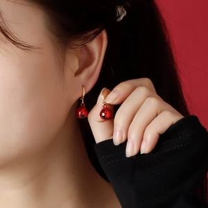 Close-up of festive red bell earrings with gold hooks worn on model with red background
