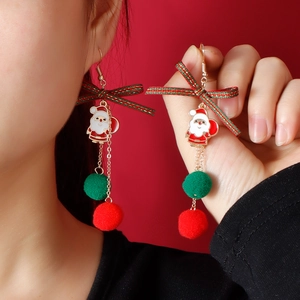 Dettaglio orecchini di Natale con fiocco, ciondolo Babbo Natale e pompon su sfondo rosso