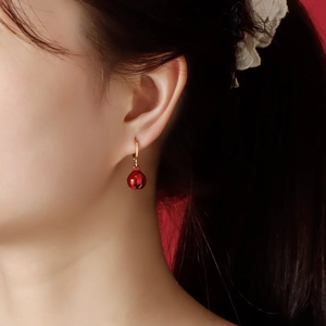 Festive red bell earrings for women with gold ear hooks on a warm red background