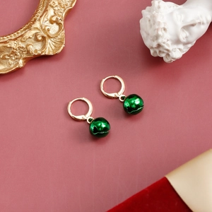 Detailed macro view of golden hoop earrings featuring festive green ball bell pendants