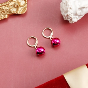 Close-up of golden hoop earrings with vibrant pink bell pendants on a vintage pink background