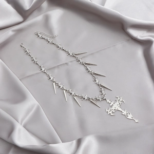 Detail of silver thorn chain necklace with punk spikes and tribal cross pendant on silk