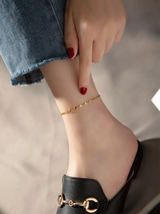 Minimalist golden chain anklet worn on ankle with denim jeans and black loafers