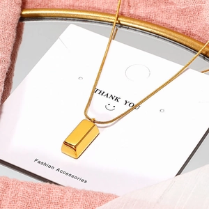 Élégant collier pendentif lingot en acier doré avec chaîne serpent sur présentoir chic